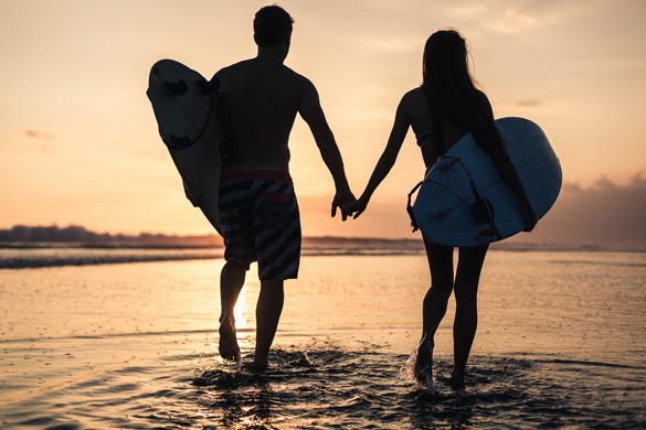 couple with surf boards at the beach sunset time - What Does The Aries Man Want In A Relationship